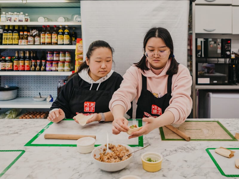 Two women learn how to make dumplings at a class.